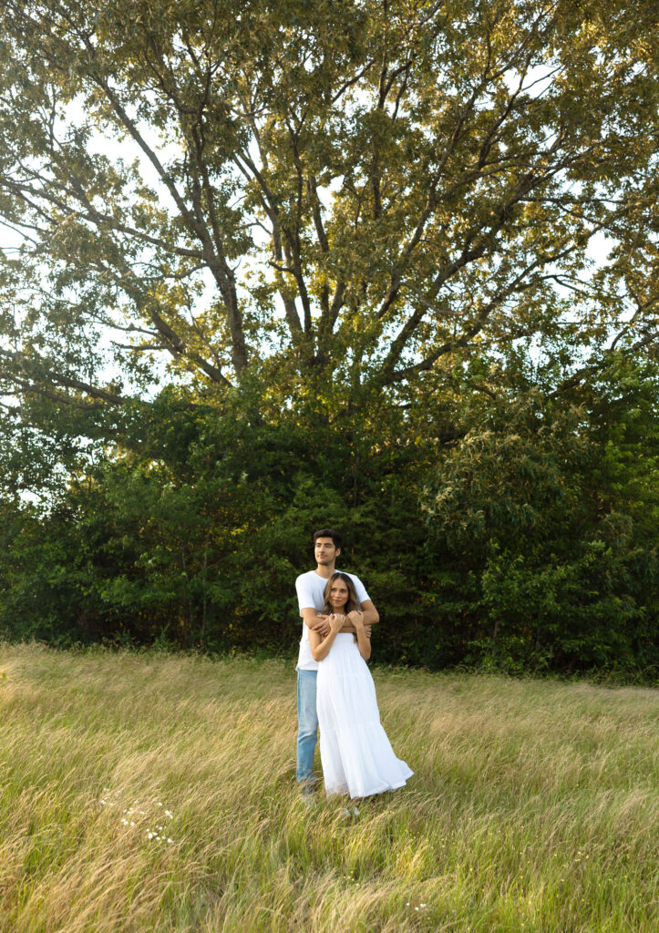 couple hugging and smiling underneath tree in field